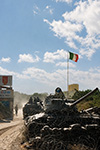 UN CARRO ARMATO M47 PARZIALMENTE INTERRATO E CIRCONDATO DA FILO SPINATO PRESIDIA L'INGRESSO FORTIFICATO DEL CAMPO ITALIANO A BALAD, MENTRE UN VEICOLO BLINDATO VCC-1 CAMILLINO VI TRANSITA ACCANTO SOTTO IL TRICOLORE.