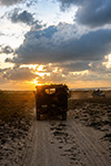 UN CONVOGLIO AVANZA LUNGO UNA PISTA SABBIOSA COSTIERA AL TRAMONTO.